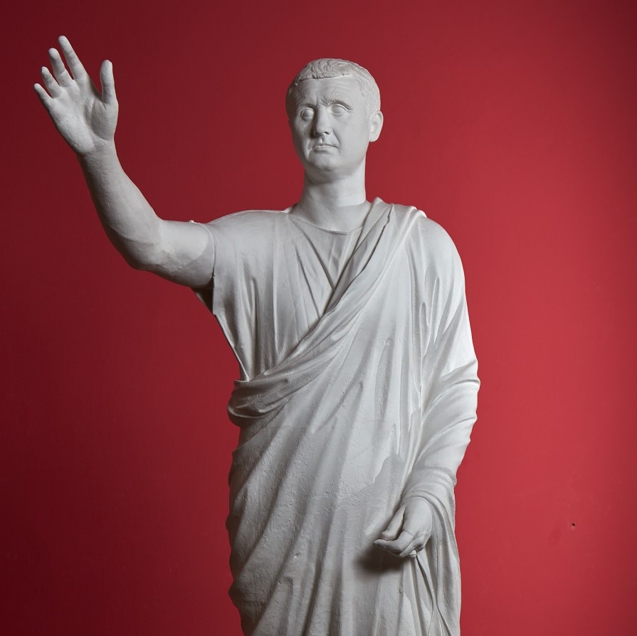 Statue eines Mannes mittleren Alters in einer Toga. Er hält die rechte Hand erhoben um eine Rede zu halten